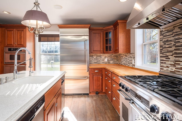 kitchen with wall chimney exhaust hood, dark hardwood / wood-style floors, high end appliances, decorative light fixtures, and decorative backsplash