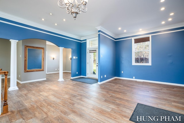 unfurnished living room featuring light hardwood / wood-style floors, an inviting chandelier, crown molding, and decorative columns