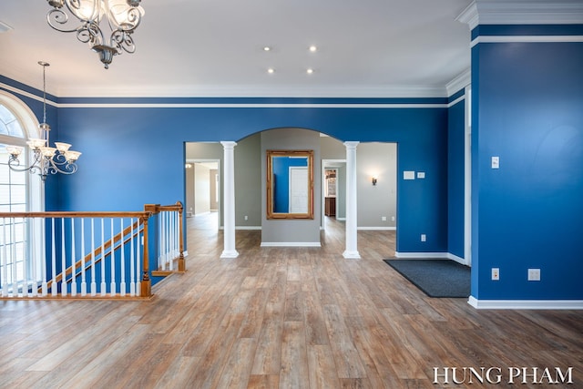 spare room featuring hardwood / wood-style floors, decorative columns, a chandelier, and ornamental molding