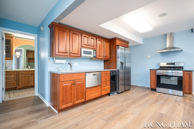 kitchen featuring wall chimney range hood, appliances with stainless steel finishes, sink, and light hardwood / wood-style floors