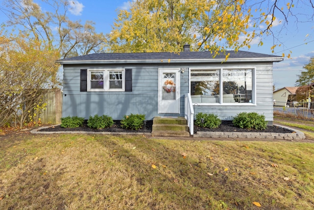 bungalow-style home with entry steps, a chimney, a front lawn, and fence