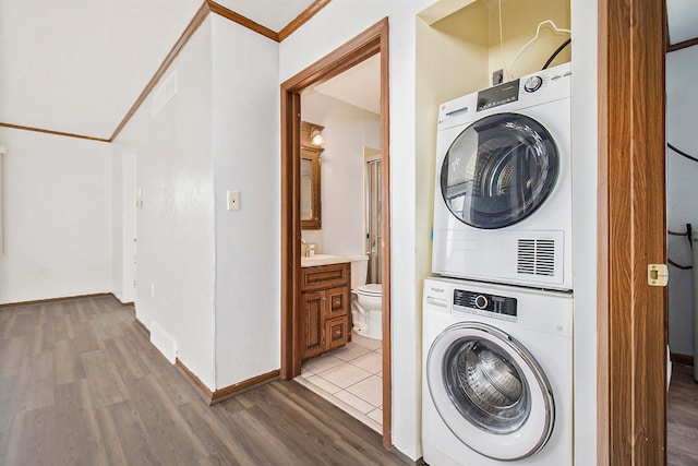 clothes washing area featuring stacked washer and clothes dryer, crown molding, and light wood-type flooring