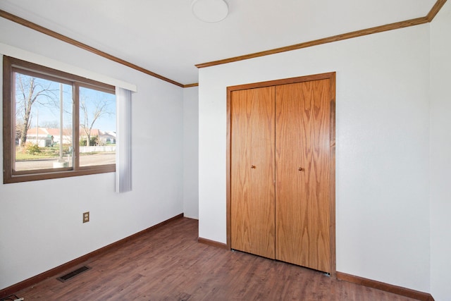 unfurnished bedroom featuring dark wood-type flooring, crown molding, and a closet