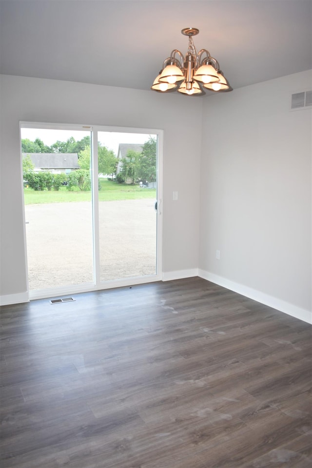 spare room featuring a notable chandelier, plenty of natural light, and dark hardwood / wood-style floors