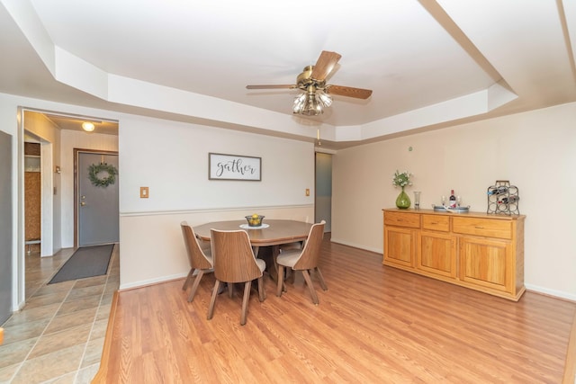 dining room with light hardwood / wood-style floors, ceiling fan, and a tray ceiling