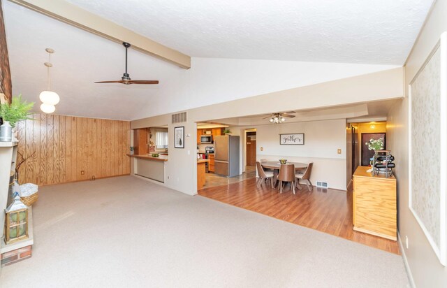 living room featuring lofted ceiling with beams, ceiling fan, wooden walls, and light hardwood / wood-style floors