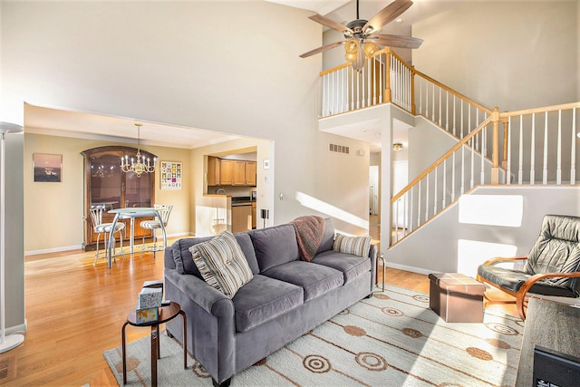 living room featuring ceiling fan with notable chandelier, light hardwood / wood-style floors, and a high ceiling