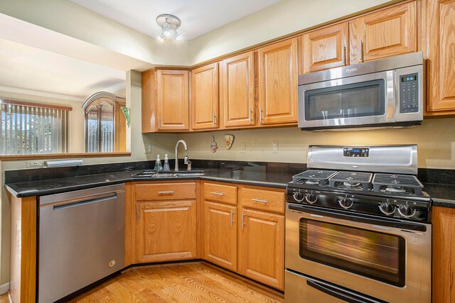 kitchen with stainless steel appliances, dark stone countertops, sink, and light hardwood / wood-style flooring