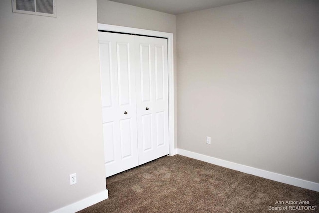 unfurnished bedroom with dark carpet and a closet