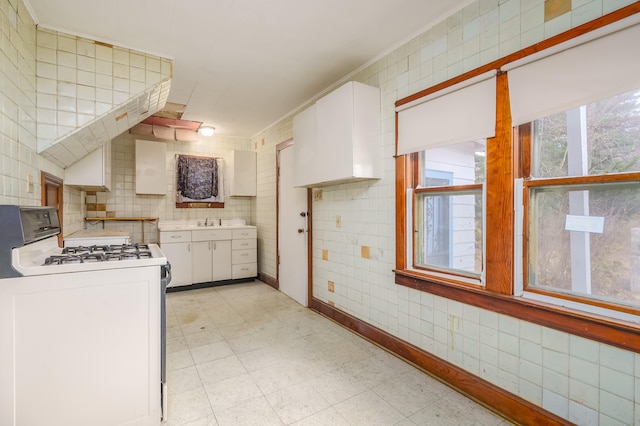 kitchen with tile walls, white range with gas cooktop, ornamental molding, white cabinetry, and sink