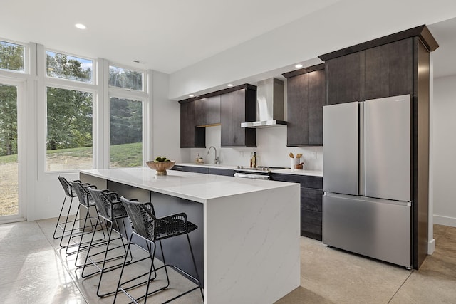 kitchen featuring stainless steel appliances, a kitchen island, light stone countertops, sink, and wall chimney exhaust hood