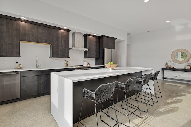 kitchen featuring stainless steel appliances, a kitchen island, wall chimney range hood, a kitchen bar, and sink