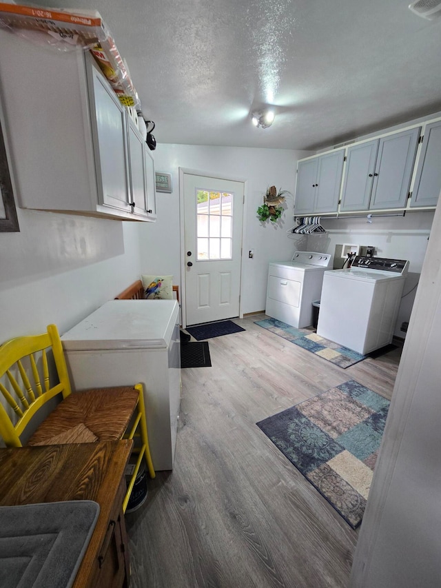 washroom featuring cabinets, separate washer and dryer, a textured ceiling, and light hardwood / wood-style flooring