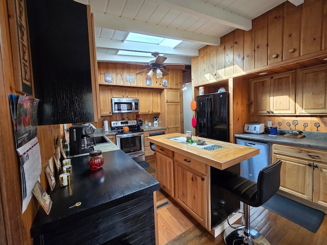 kitchen featuring appliances with stainless steel finishes, beam ceiling, wood counters, a skylight, and a center island