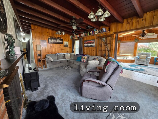 living room featuring wooden walls, ceiling fan with notable chandelier, tile patterned flooring, and beam ceiling