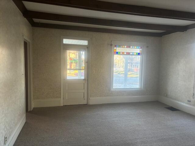 carpeted empty room with beamed ceiling