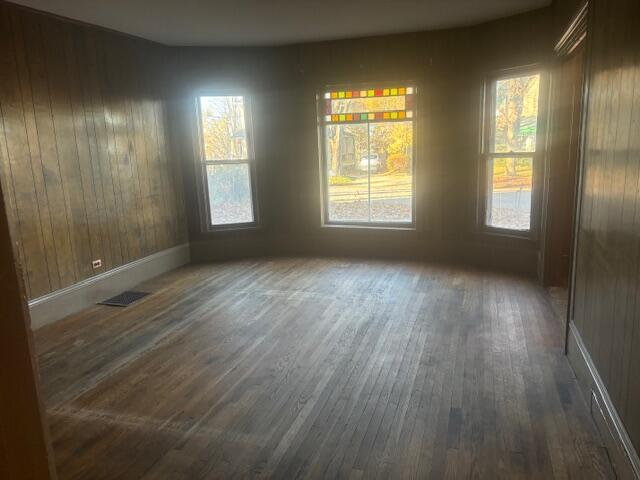 unfurnished dining area with dark hardwood / wood-style flooring, wood walls, and a healthy amount of sunlight