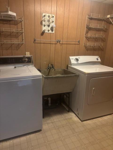 laundry area featuring wooden walls, sink, and independent washer and dryer