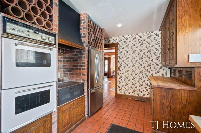 kitchen featuring light tile patterned flooring, stainless steel refrigerator, and white double oven