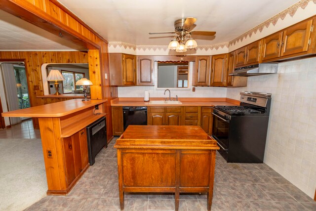 kitchen featuring ceiling fan, sink, kitchen peninsula, wooden walls, and black appliances