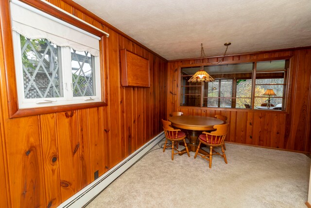 carpeted dining space with a textured ceiling, a baseboard heating unit, and wood walls