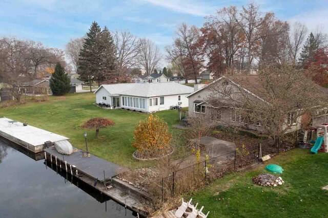 rear view of house featuring a sunroom, a water view, and a lawn