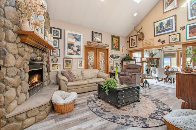 living room with a stone fireplace, light hardwood / wood-style flooring, and high vaulted ceiling