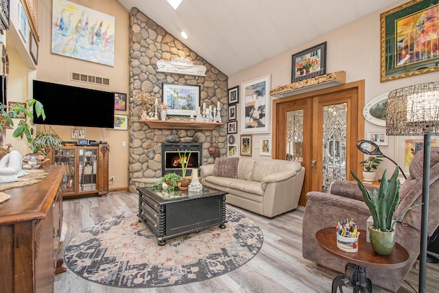 living room featuring high vaulted ceiling, a stone fireplace, french doors, and light hardwood / wood-style floors