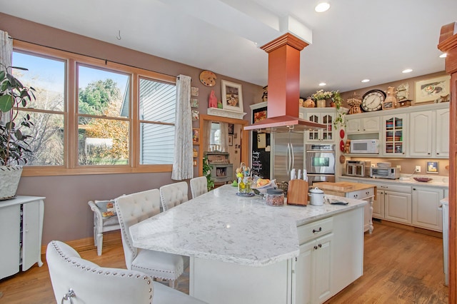 kitchen with stainless steel appliances, light hardwood / wood-style flooring, a kitchen island, decorative columns, and white cabinets