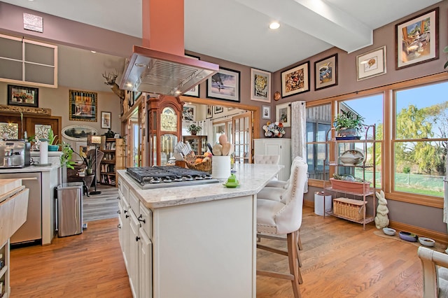 kitchen with light hardwood / wood-style floors, stainless steel gas cooktop, a kitchen bar, white cabinets, and island exhaust hood