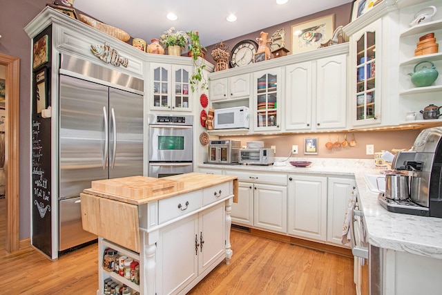 kitchen featuring appliances with stainless steel finishes, light stone countertops, a center island, white cabinets, and light wood-type flooring