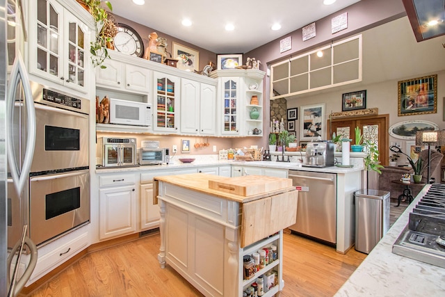 kitchen featuring light hardwood / wood-style floors, white cabinetry, light stone counters, appliances with stainless steel finishes, and a kitchen island