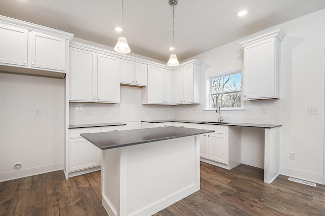 kitchen featuring visible vents, a kitchen island, backsplash, dark wood-style flooring, and a sink