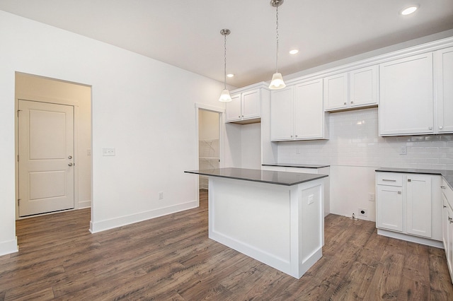 kitchen featuring dark wood-style flooring, white cabinetry, decorative backsplash, a center island, and dark countertops