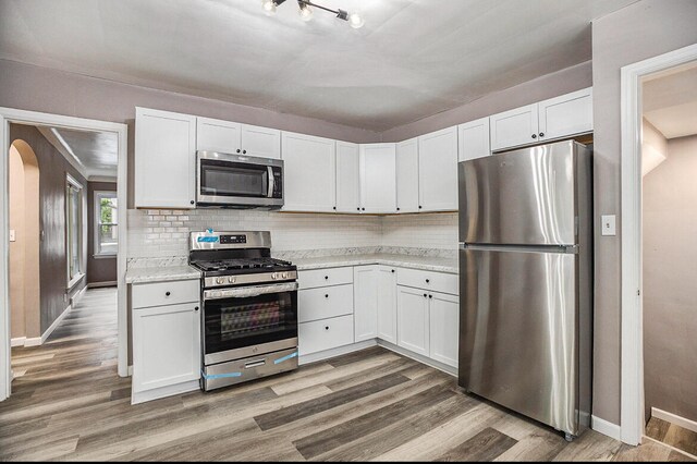 kitchen with appliances with stainless steel finishes, wood-type flooring, and white cabinets