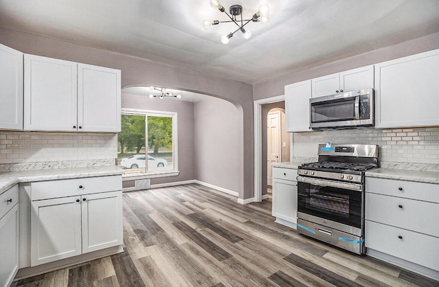 kitchen featuring white cabinets, decorative backsplash, appliances with stainless steel finishes, and hardwood / wood-style floors