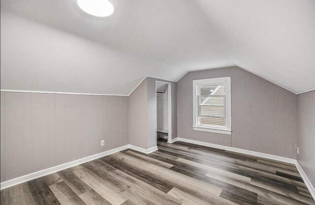 additional living space featuring wood walls, lofted ceiling, and hardwood / wood-style floors