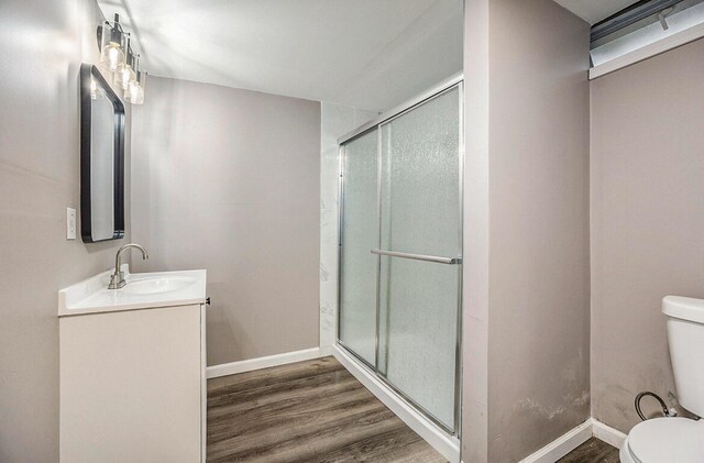 bathroom with hardwood / wood-style flooring, a shower with shower door, vanity, and toilet