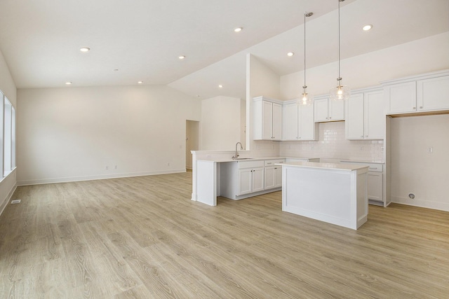 kitchen with a sink, white cabinets, open floor plan, light countertops, and pendant lighting