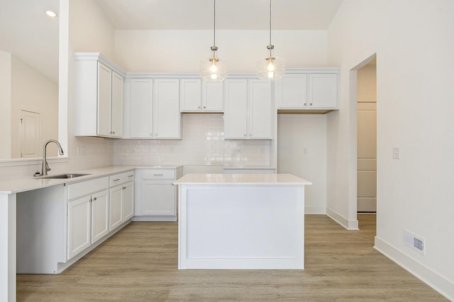 kitchen with white cabinets, decorative light fixtures, a center island, light countertops, and a sink