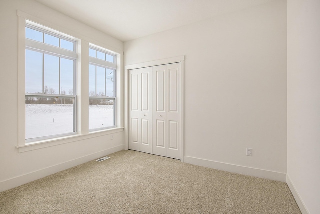 unfurnished bedroom featuring a closet, light carpet, visible vents, and baseboards