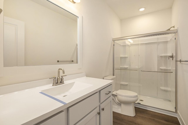 bathroom with a stall shower, toilet, wood finished floors, vanity, and recessed lighting