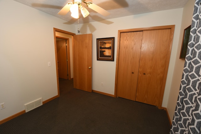 unfurnished bedroom featuring ceiling fan, a textured ceiling, a closet, and dark carpet