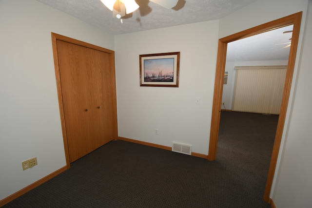 interior space with ceiling fan, a textured ceiling, a closet, and dark colored carpet