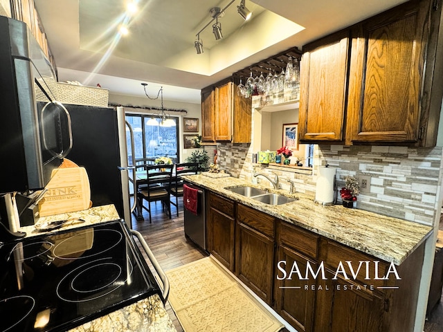 kitchen featuring backsplash, stainless steel appliances, a tray ceiling, sink, and light hardwood / wood-style flooring