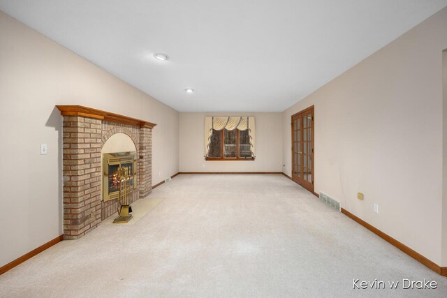 unfurnished living room featuring french doors, light carpet, and a brick fireplace