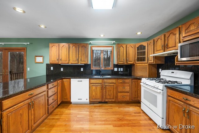 kitchen featuring backsplash, white appliances, sink, light hardwood / wood-style flooring, and dark stone countertops