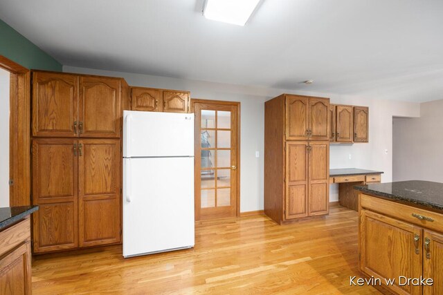 kitchen featuring white fridge, light wood-type flooring, built in desk, and dark stone countertops