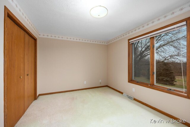 unfurnished bedroom with light colored carpet, a textured ceiling, and a closet