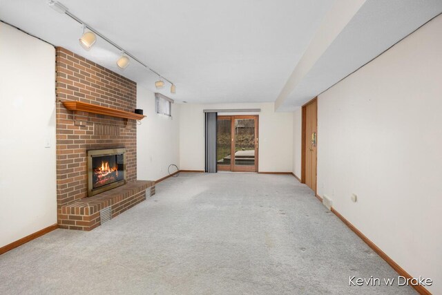 unfurnished living room with rail lighting, light colored carpet, and a brick fireplace